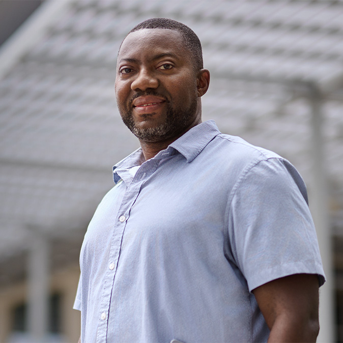  Kofi stojí venku a usmívá se do fotoaparátu.