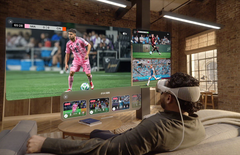 Apple Vision Proを装着した人物がリビングのソファに座っている。その目の前には大きなスクリーンでビデオが表示され、その横に2つの小さなスクリーンがある。それぞれ異なるスポーツイベントが映し出されている。大きなスクリーンの下には「さらに追加」と上部に書かれた選択ウィンドウが表示されている