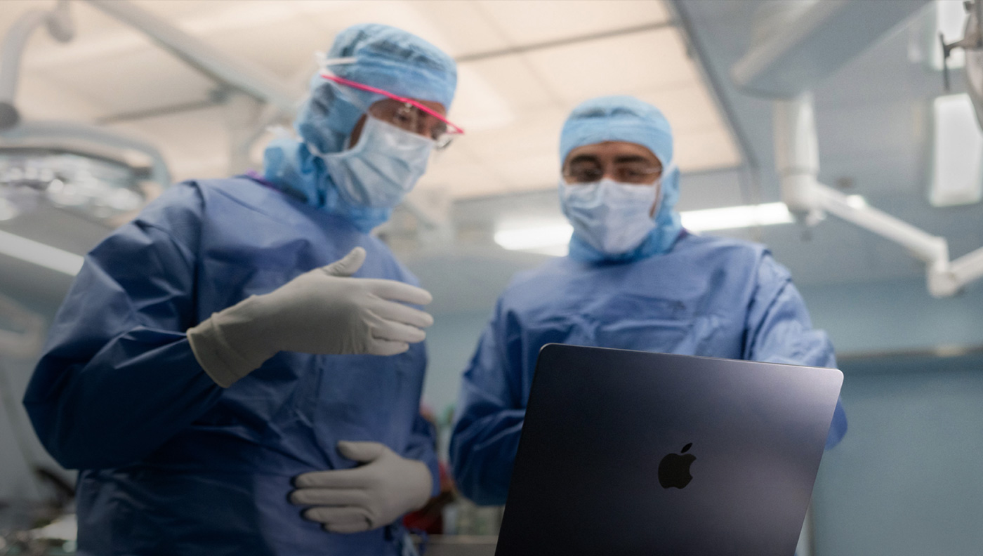 兩位外科醫生在手術室，討論 MacBook Pro 螢幕上的內容。