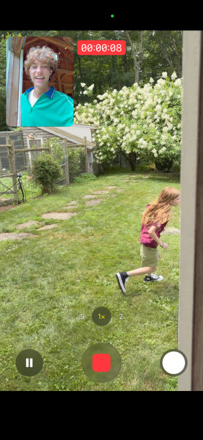 Schermo di iPhone 17 con la funzione Acquisizione doppia che usa la fotocamera frontale e quella posteriore per registrare simultaneamente una bambina che corre e un ragazzo che la guarda